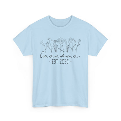 Flatlay of pink ‘Promoted to Grandma 2025’ T‑shirt styled with flowers, ideal pregnancy reveal gift flat presentation.
